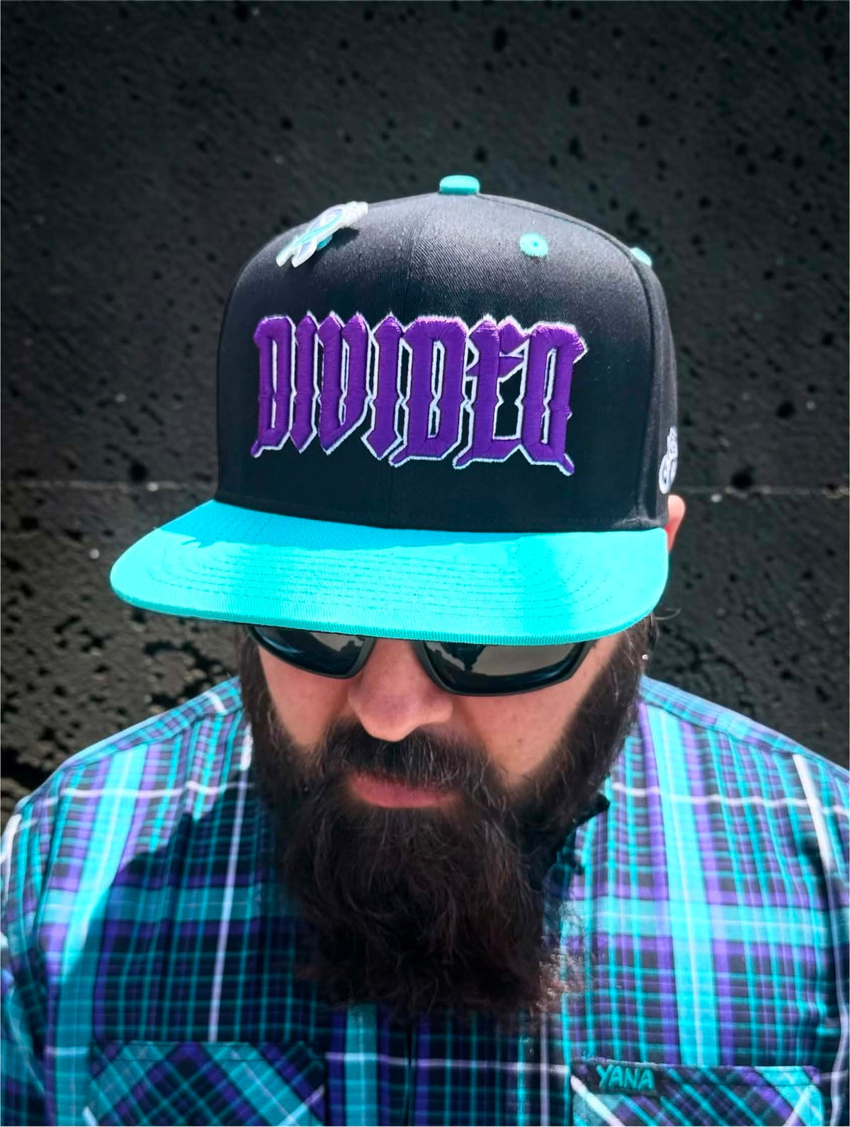Black Divided Flannel Co. YANA snapback worn with matching teal and purple flannel